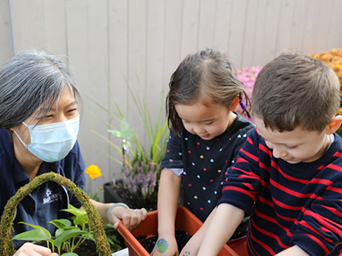 teacher with mask on looking over children playing in garden