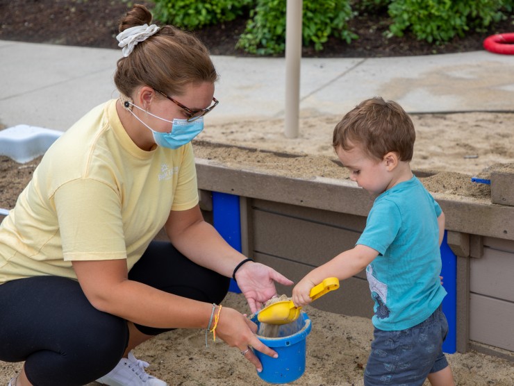 teacher playing with child in sandbox