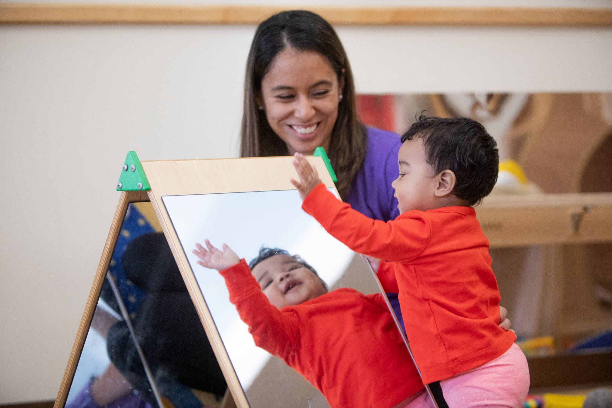 A Bright Horizons teacher and a toddler looking into a mirror