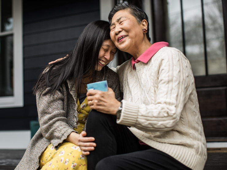 A woman and elderly mom hugging on a porch.