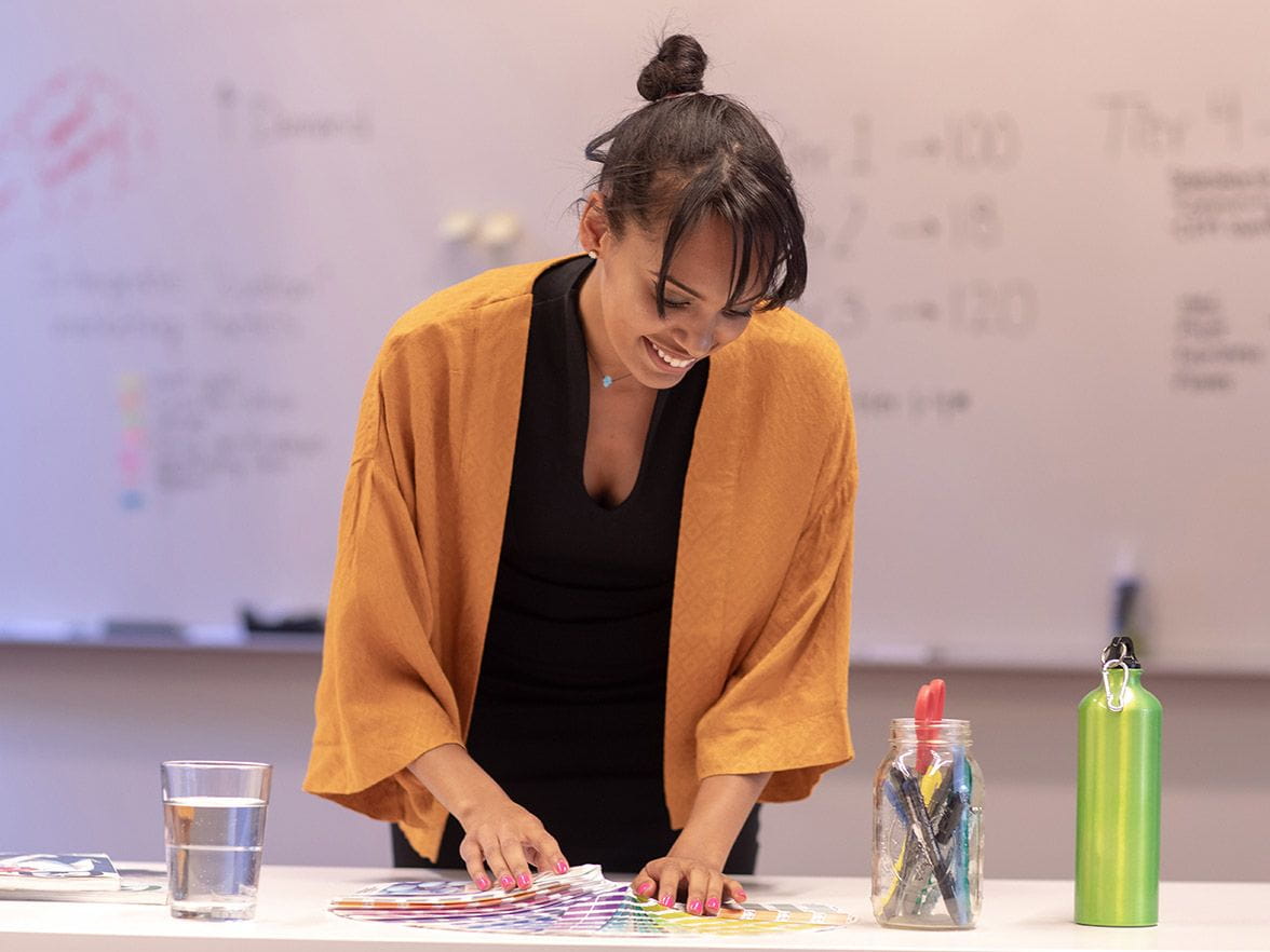 Teacher smiles and looks down in front of white board | Bright Horizons