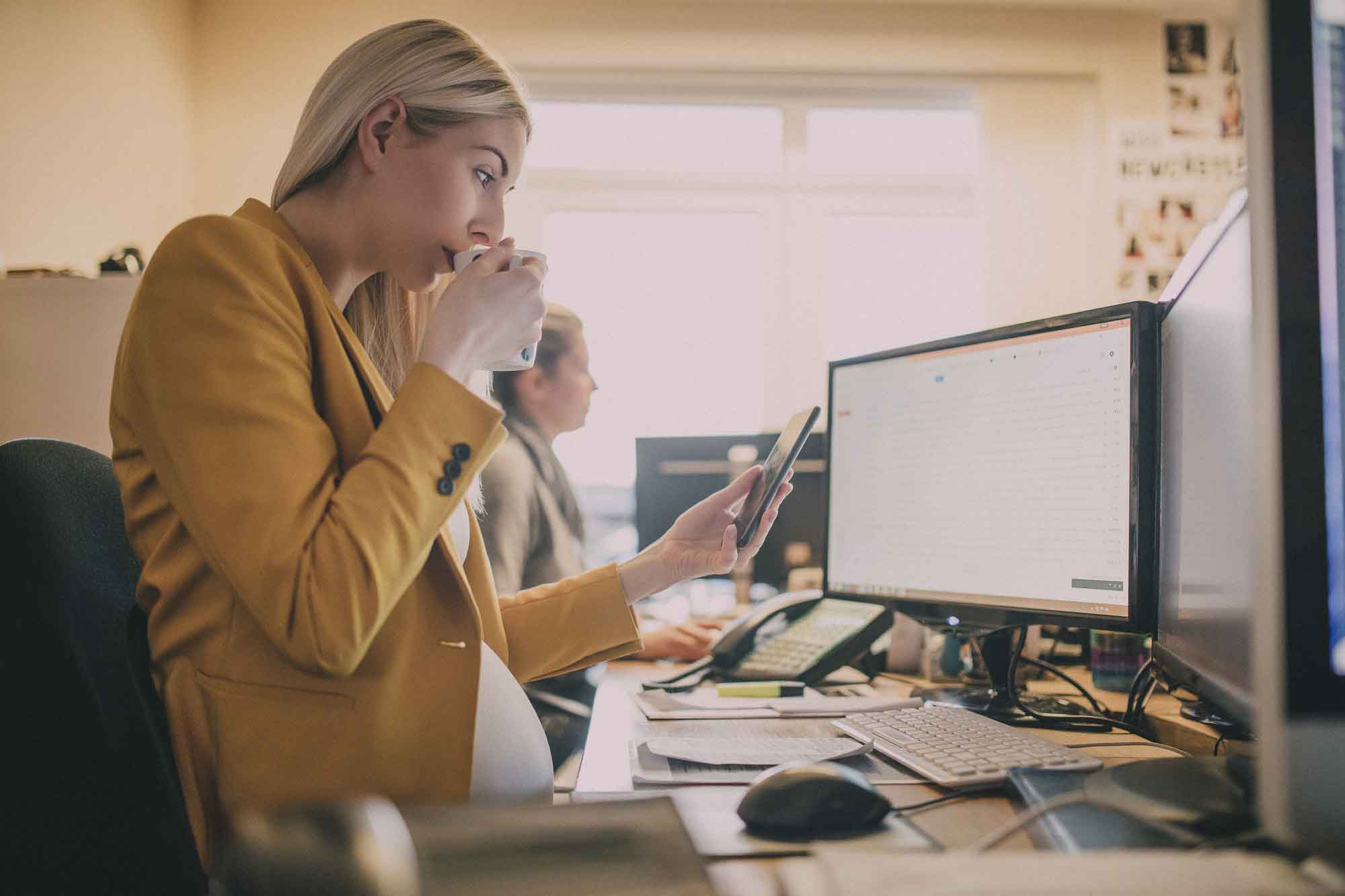 A pregnant woman sitting at her desk. 