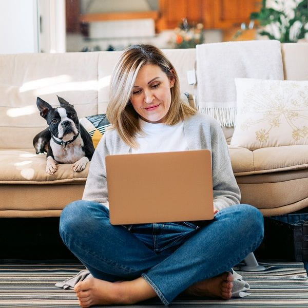 woman sitting on floor working on laptop with dog