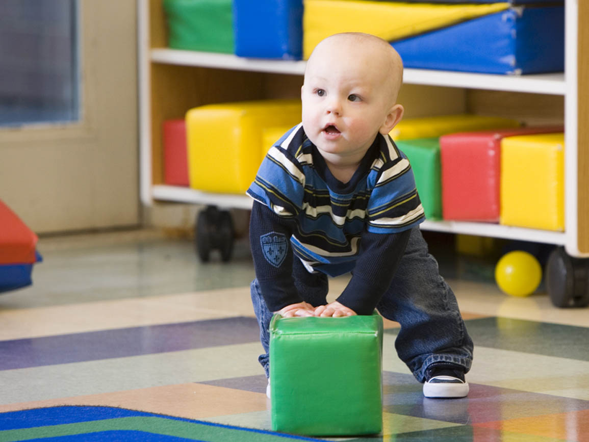 Toddler boy pushing soft green block in gym