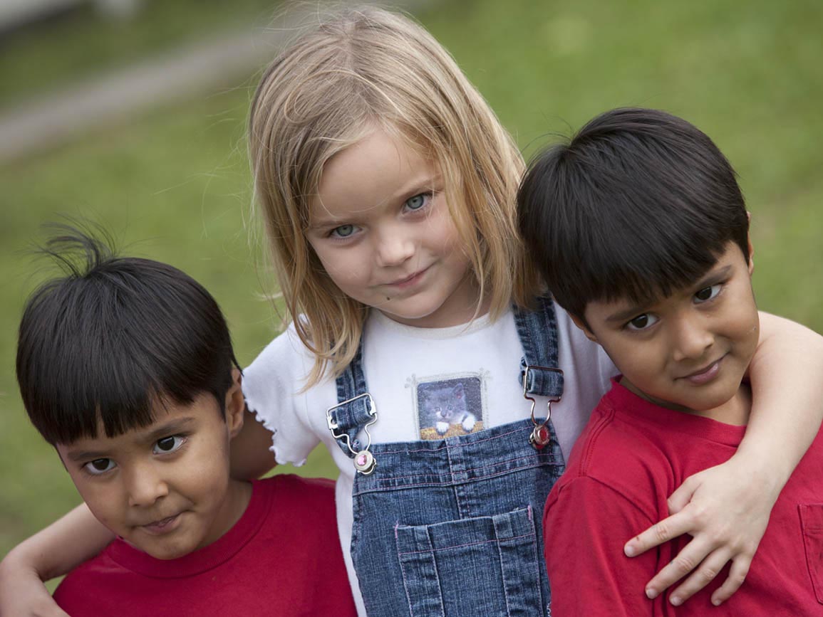 Preschool aged girl with her arms around twin preschool boys