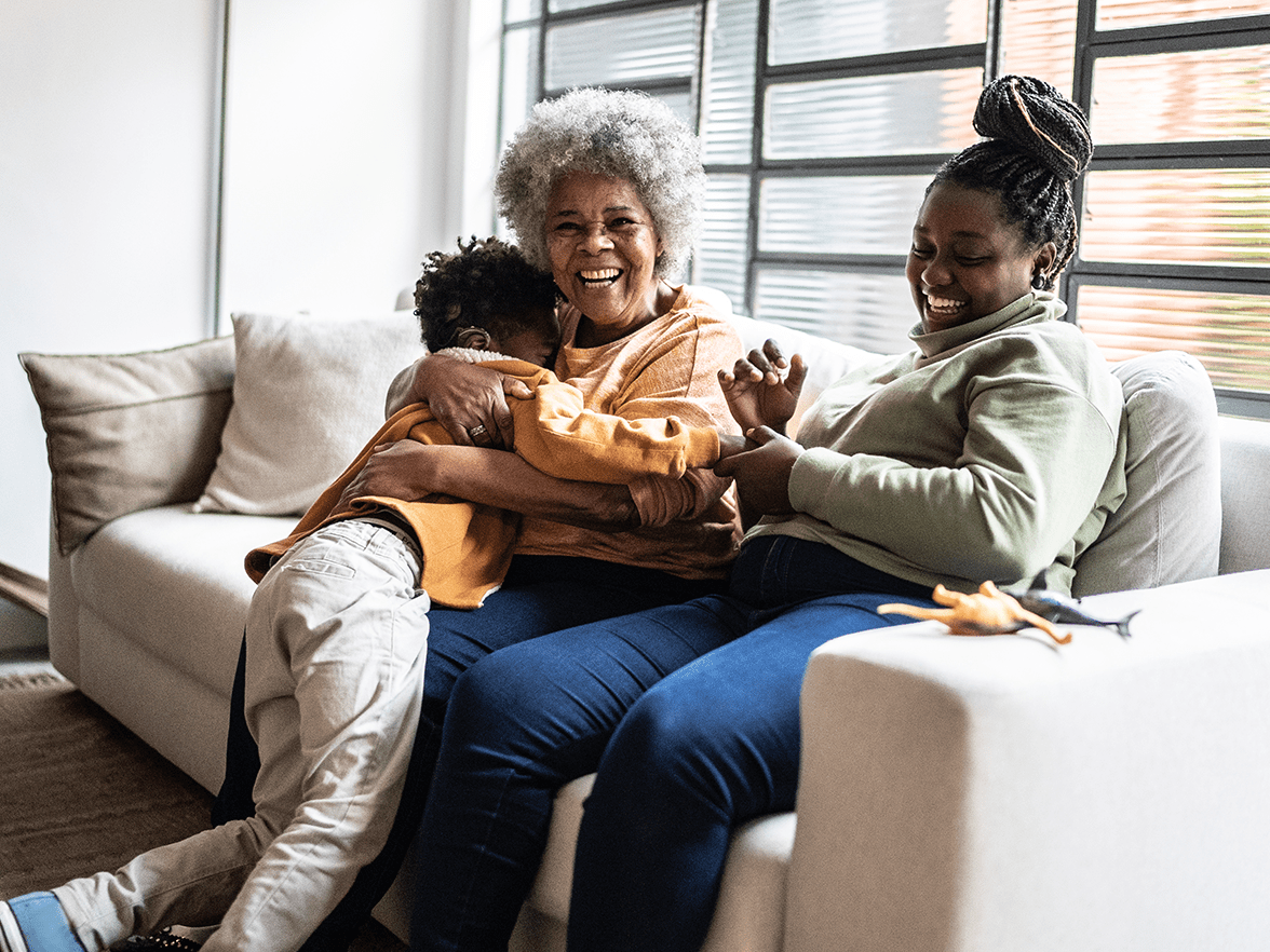 A woman, grandmother and child laughing on couch