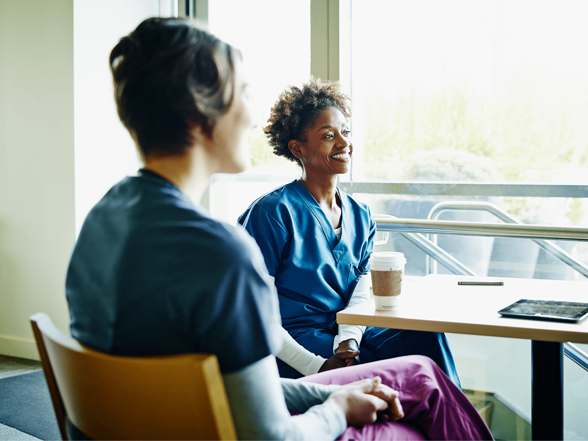 Two women sitting at a table in scrubs