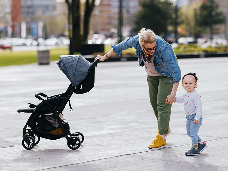 Mother holding her preschooler's hand while pushing a carriage with her other hand